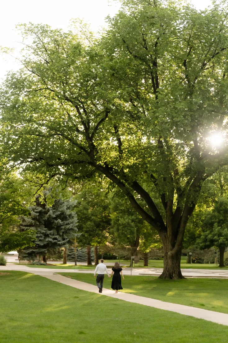 Brianna and Evan walking hand in hand down a tree-lined park path
